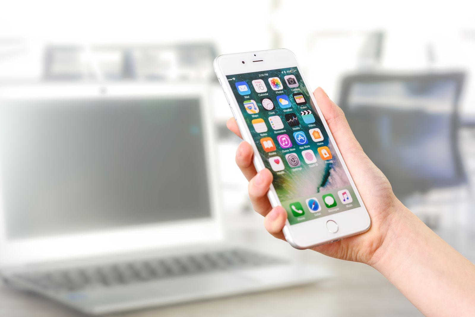Une main tient un smartphone devant un ordinateur portable